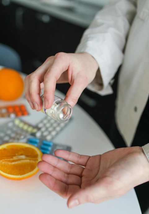Close-up of person taking vitamins and pills beside fresh orange, emphasizing health and immunity.