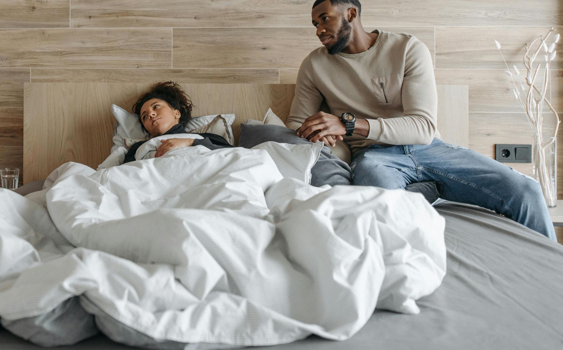 A healthcare worker caring for a sick person in bed, with a supportive partner nearby.