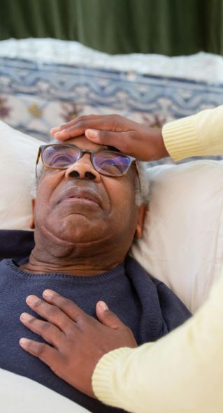 A caregiver attending to an elderly man in bed, providing comfort and support.