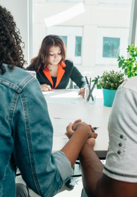 Couple holding hands during an adoption meeting with a social worker in an office setting.